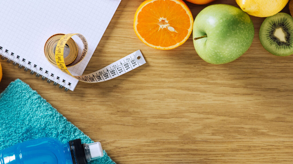 A tape measure and workout gear along with various fruits symbolize a weightloss diet